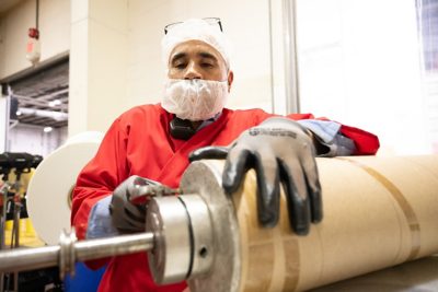 A man in red shirt and gloves is handling a roll of paper.