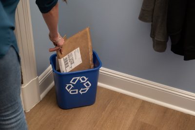 una mujer está colocando un sobre para envíos con burbujas en un contenedor de reciclaje azul