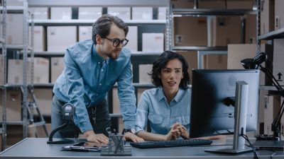 Ein Ingenieur und eine leitende Angestellte besprechen und suchen nach Online-Bauplänen auf tragbaren Computern.