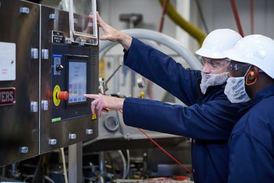 Trabalhadores com uniforme azul e capacete branco usam equipamentos