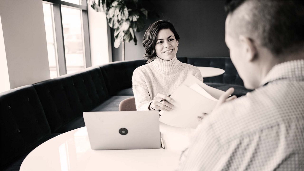 A man and woman talking at a table in an office.