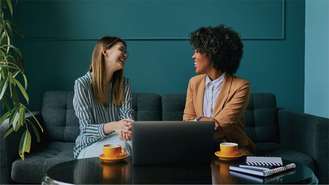 Two smiling employees have a meeting over coffees.