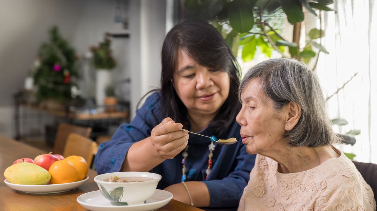 woman helps feed other older woman