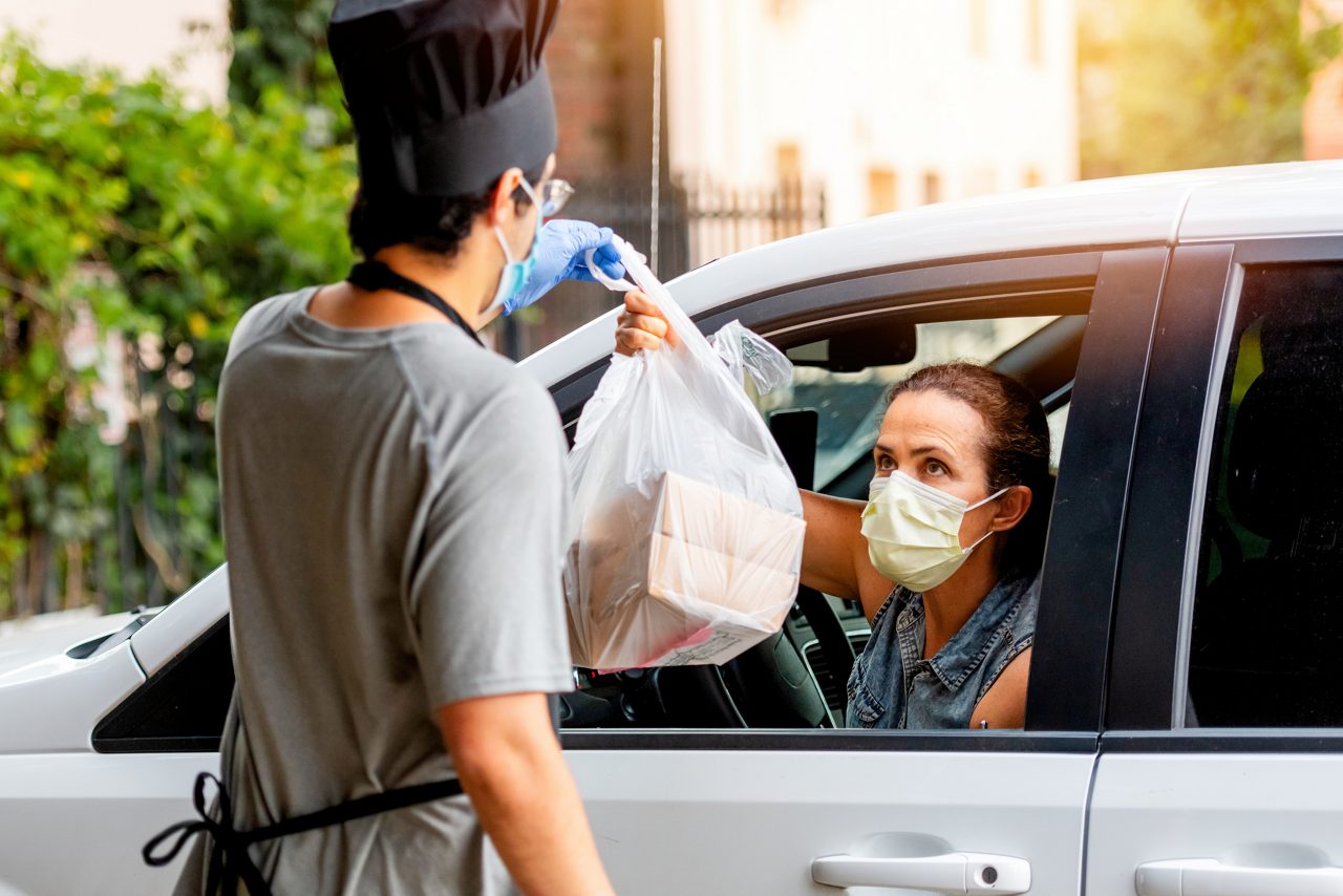 working handing takeout food to customer in car