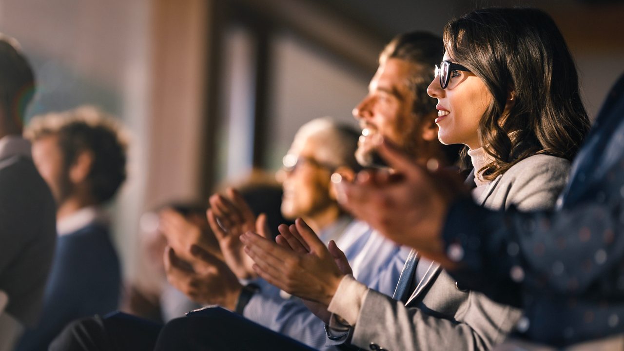 a row of people clapping while looking towards a stage