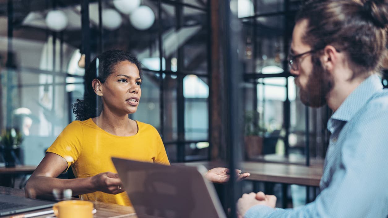 A man and woman talking at a table in an office.