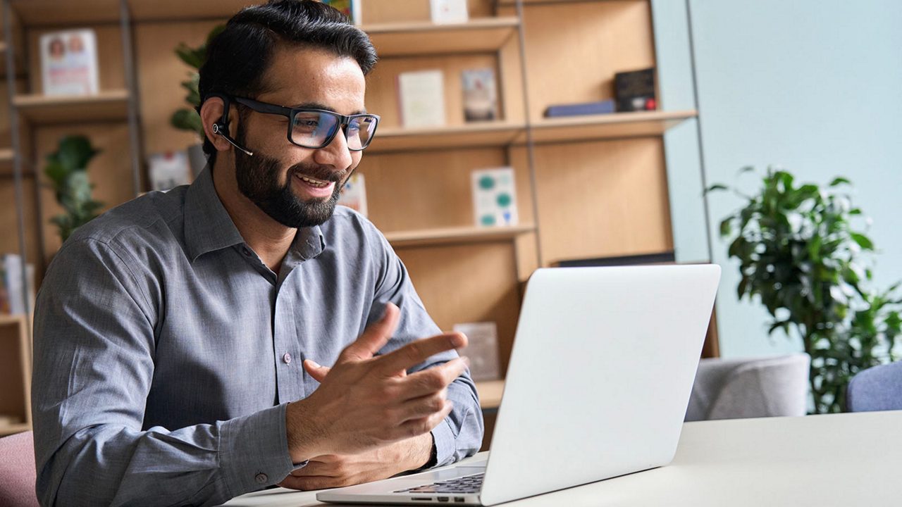 Male professional with headset on and looking at  laptop and smiling as he engages with a video conference call 