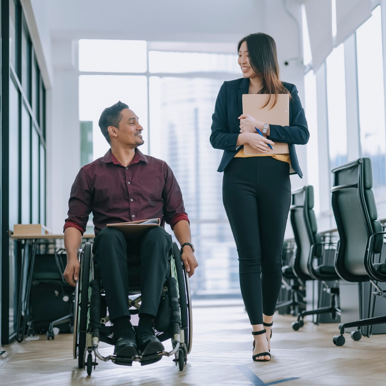 man in a wheelchair in a hallway with female coworker