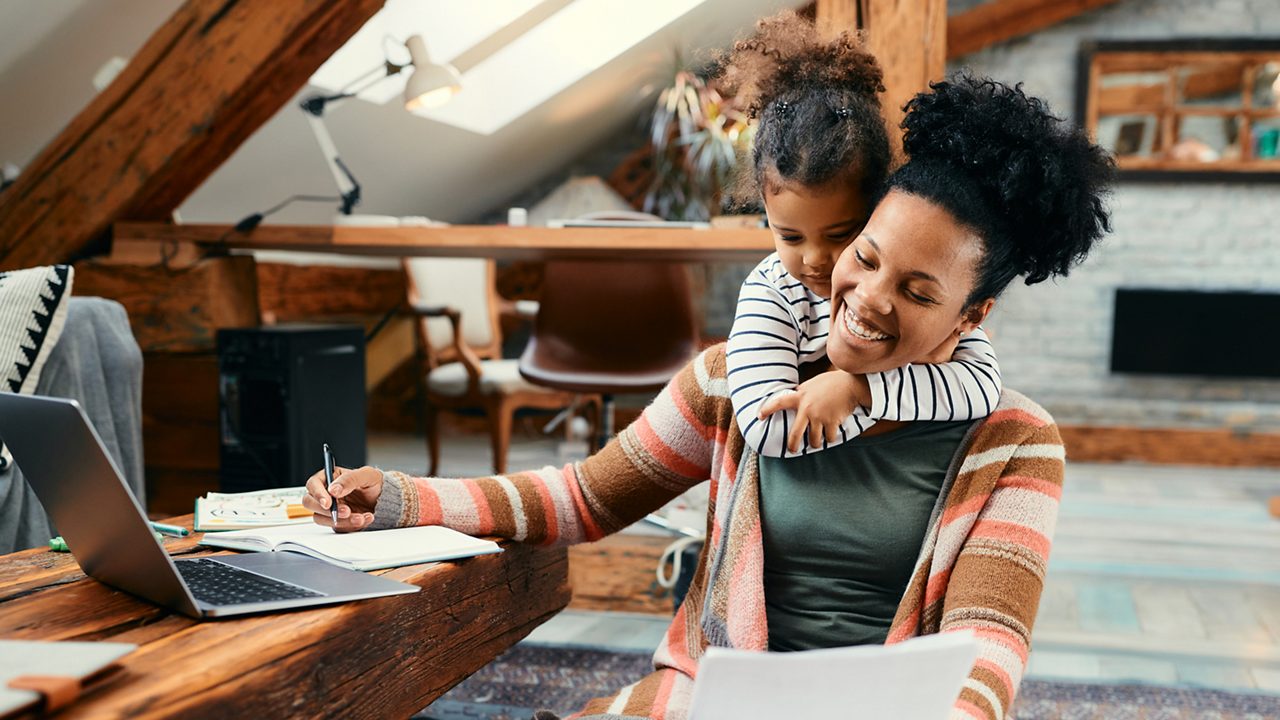 woman at home working with her daughter on her shoulders