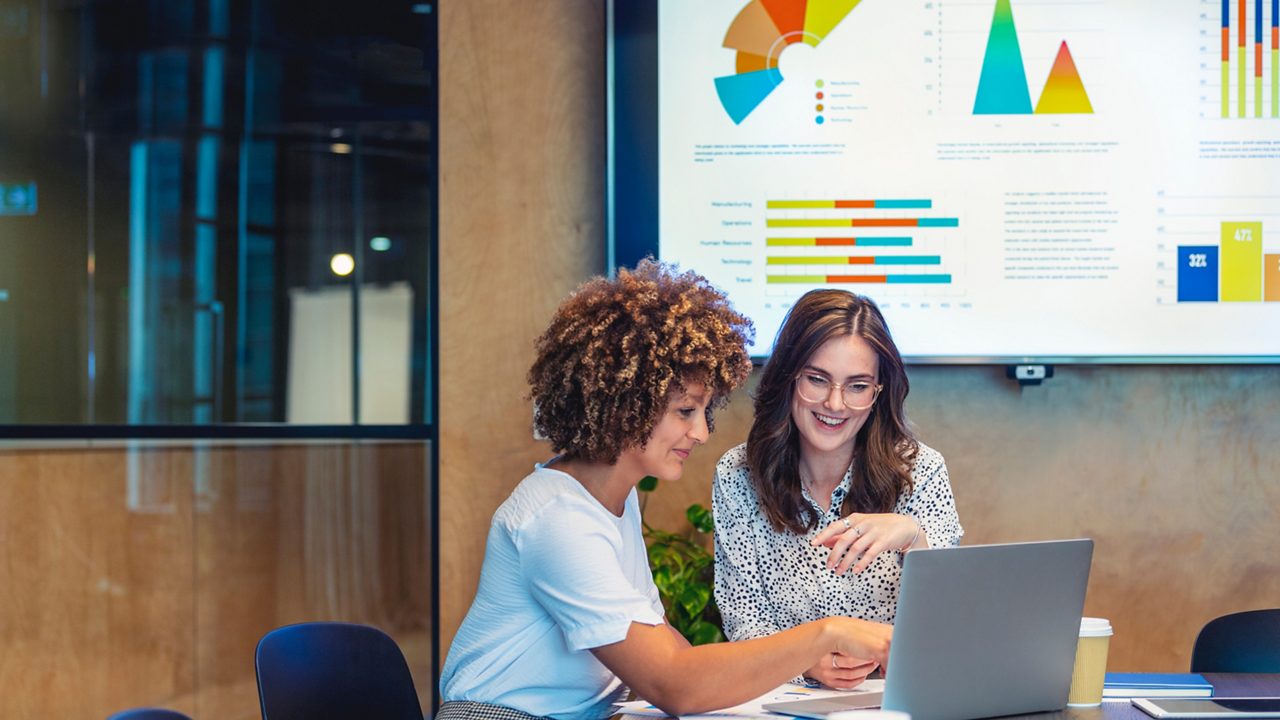 Two women enthusiastically discussing something while referencing a laptop