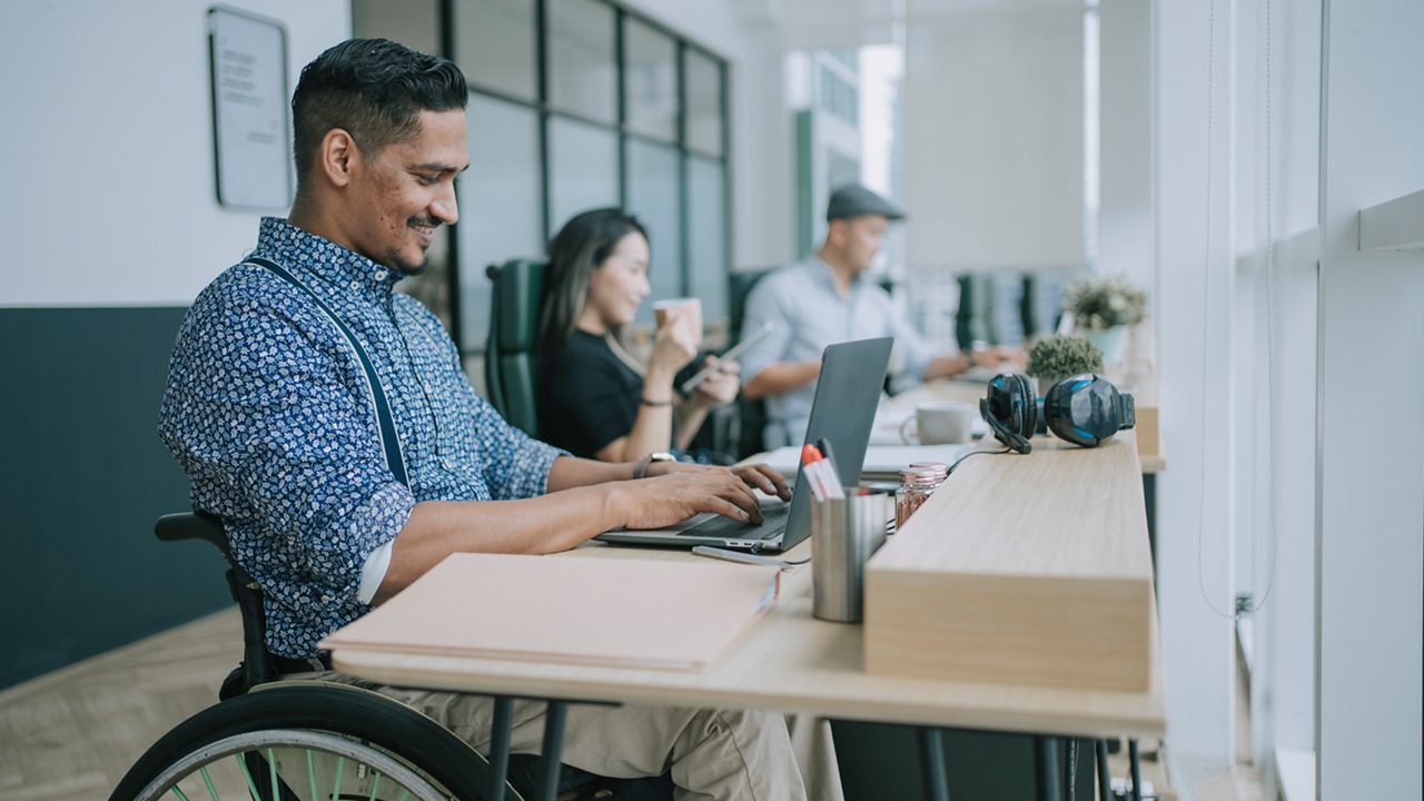 a man in a wheelchair works at his desk alongside his coworkers