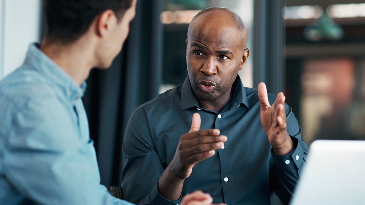 a man passionately talks with his hands as he speaks to another man