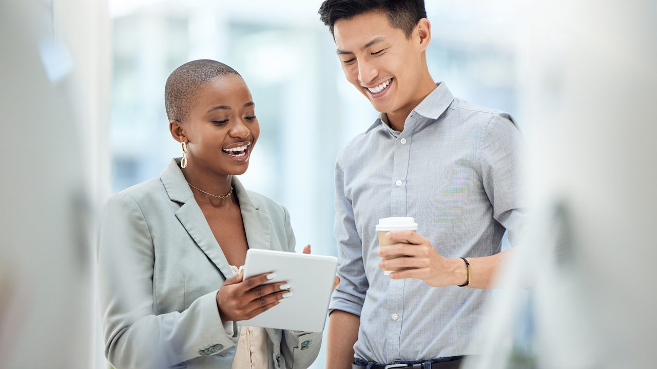 Two happy colleagues chatting and looking at a tablet device