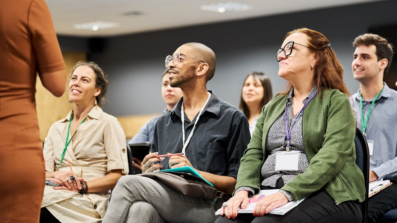 a group of men and women sitting in a conference room listening to a speaker