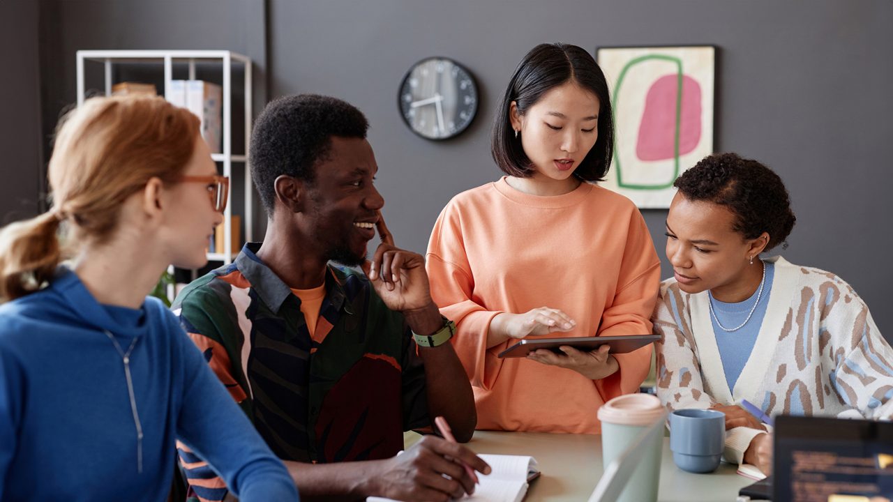 a group of casually dressed coworkers collaborates over a tablet