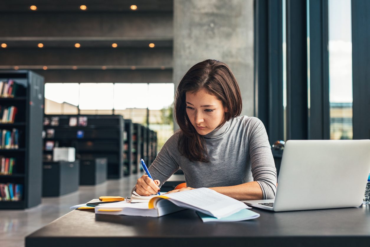 Woman writing in a notebook in a large public library.