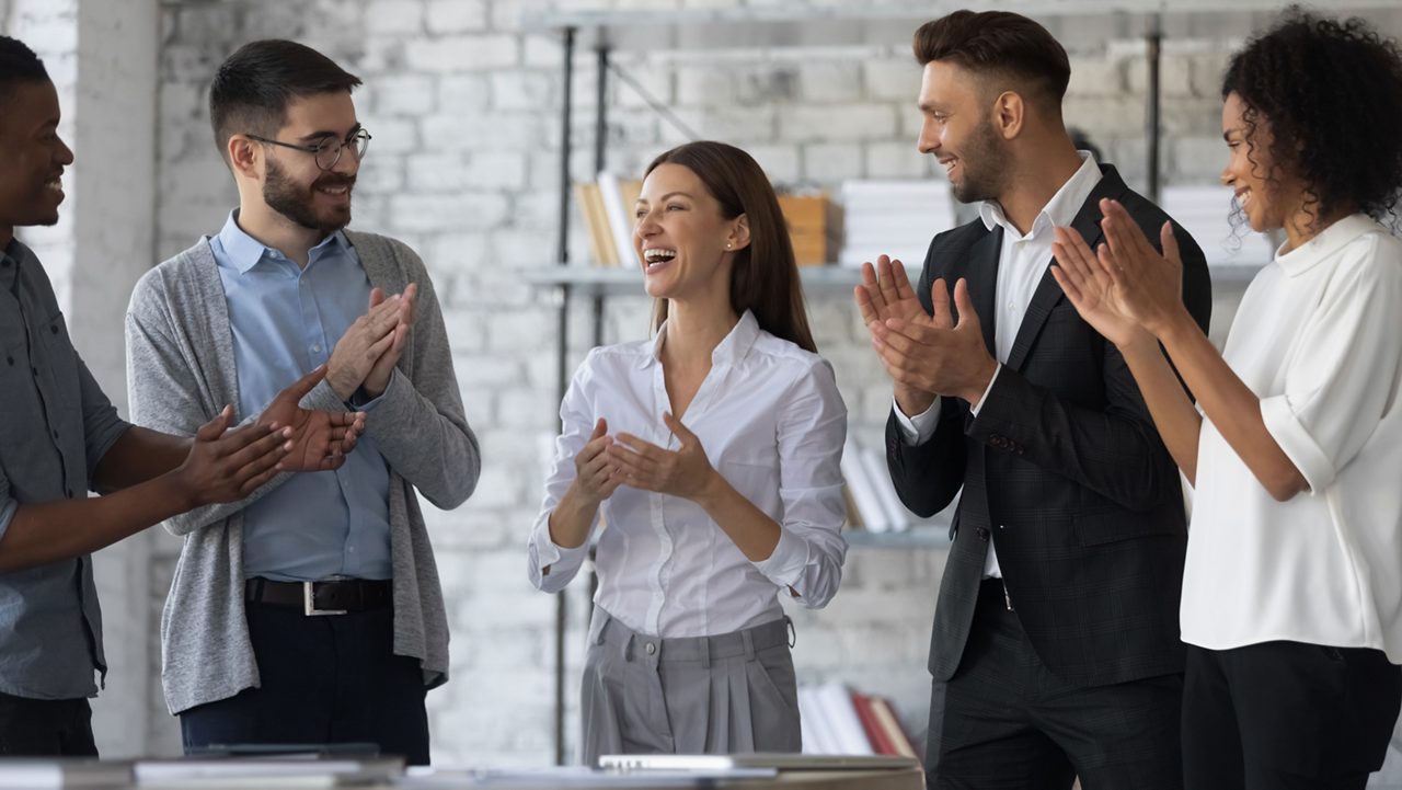 Friendly diverse employees congratulating businesswoman with business achievement, great work results or job promotion, business people applauding and cheering, standing in modern office