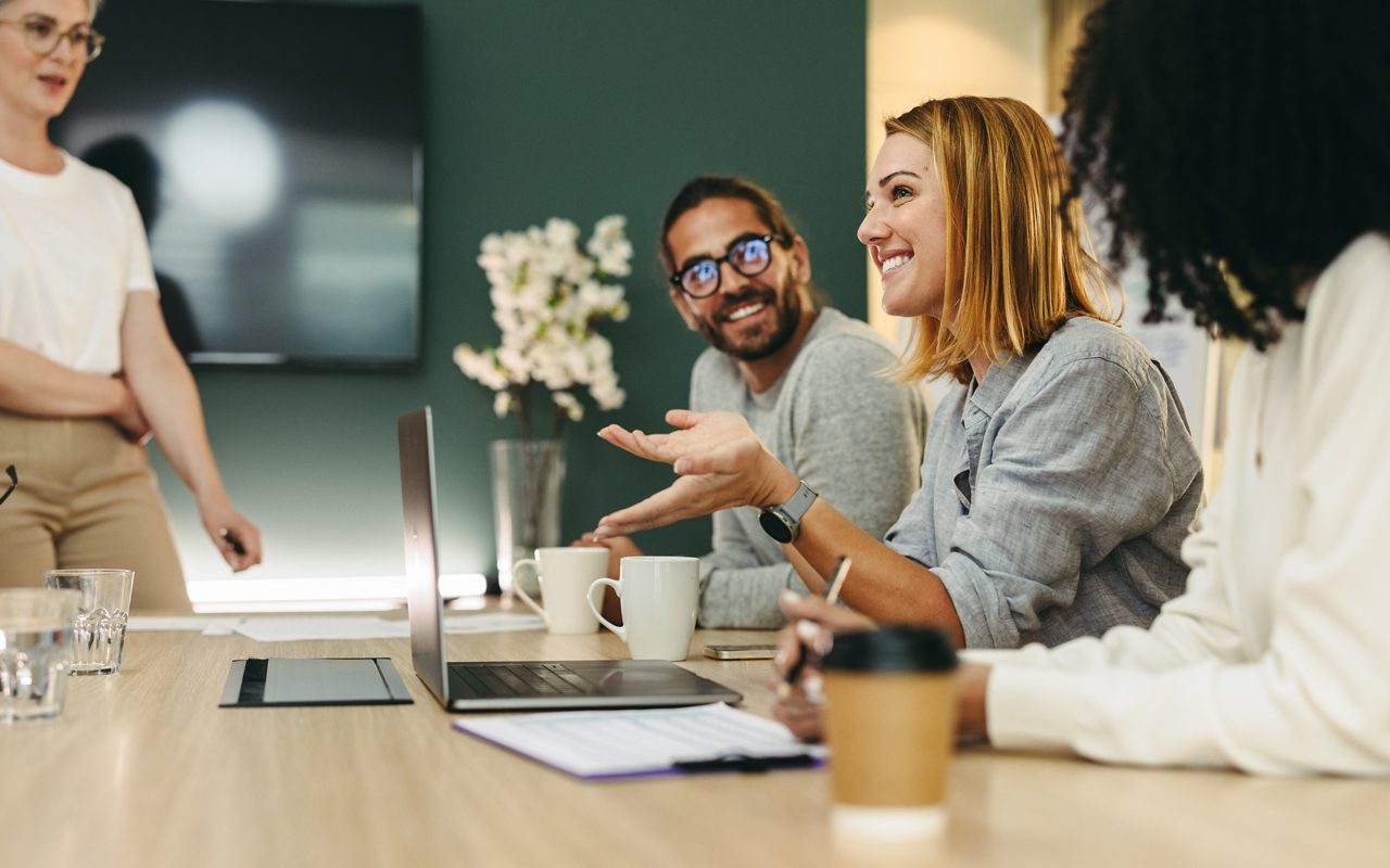 Cheerful businesswoman having a discussion with her colleagues in a boardroom. Group of happy businesspeople sharing ideas during a meeting in a modern workplace.