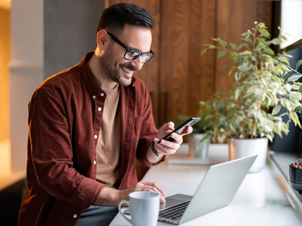 Man smiles on his phone while working on a laptop.