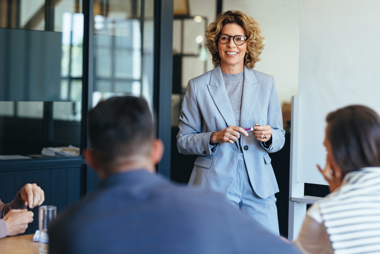 Mature business woman having a discussion with her team. Woman leading a meeting in an office. Business woman presenting her ideas in an office. Group of professionals planning a project.