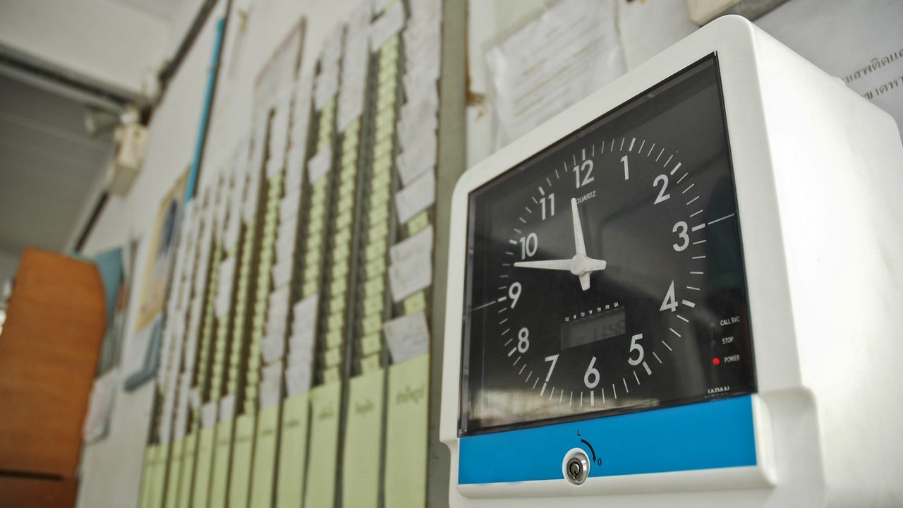 A time clock and time cards hanging in slots next to it.