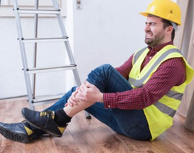 A laborer seated next to a ladder on the floor clutches their shin in pain