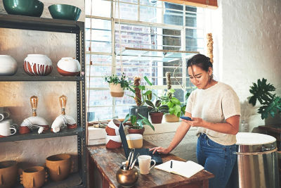 Click image of woman in home office space surrounded by her ceramic art checking her laptop to navigate to page: Connect with us