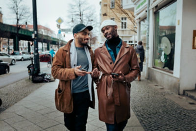 Friends walking down sidewalk conversing about something on their phones