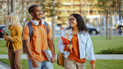 Diverse college students walking on university campus with notebooks and backpacks on sunny day