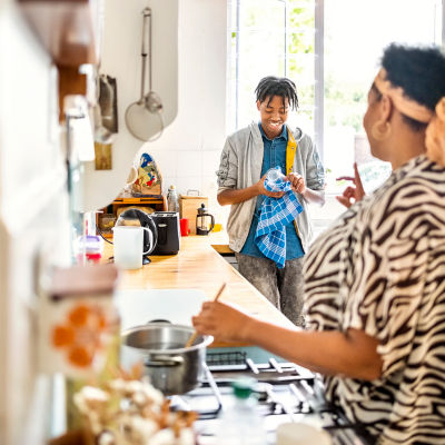 A mother standing in the kitchen with a mixing bowl, having a conversation with a teenaged boy about education costs.