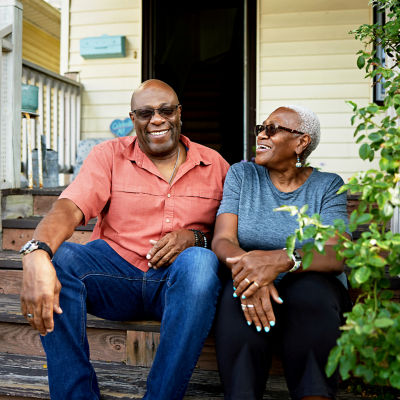 Man and woman on porch stairs, smiling and laughing together, enjoying a cheerful moment in retirement.
