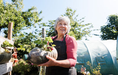 A woman holding a potted plant in front of a greenhouse