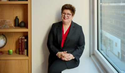 Emily, professionally dressed, leaning against a window sill 