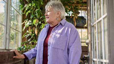 A retirement-age woman standing indoors gazes outside.