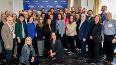 Group photo of 2025 TIAA Institute Fellows in business attire, standing together against a backdrop with TIAA Institute logos.