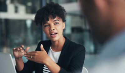 Professional woman in black blazer making an animated gesture while speaking.