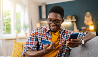 A young man examining a credit card and holding a cell phone.