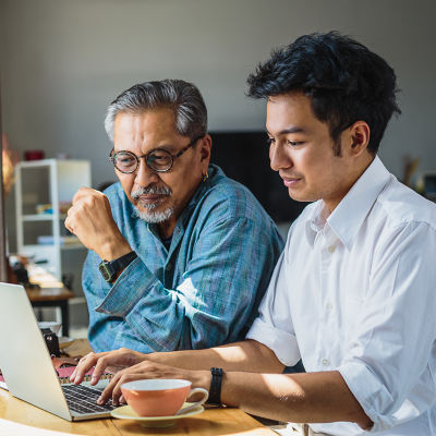 An older man sitting with a younger man looking at a laptop computer.