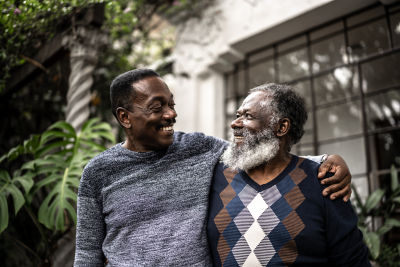 Elderly father and son with the son's arm wrapped around his father's shoulder