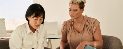 Two professional women review documents related to initiating a fee collection strategy for an MEP at a table.