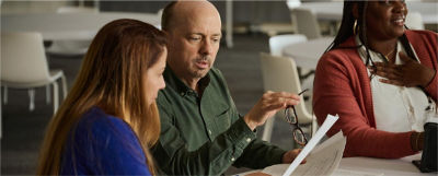 Three professionals discuss PlanFocus tools for managing MEP services, with one woman pointing at a tablet screen