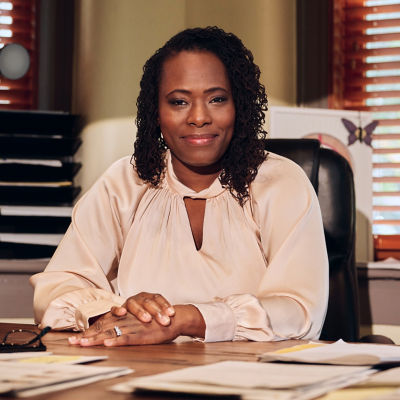 Smiling woman sitting at a desk with her hands folded on top of it