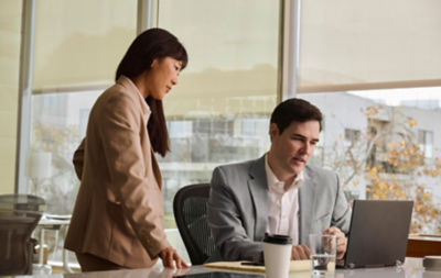 A man is sitting at a laptop while a woman looks over his shoulder