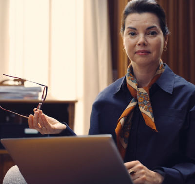 Woman sitting at a laptop holding her glasses to the side