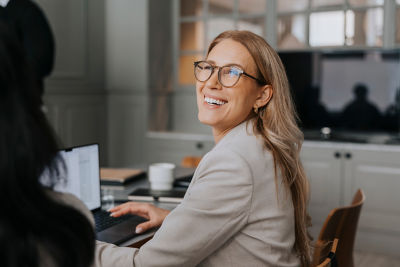 Woman with glasses smiling as she looks up from her computer.