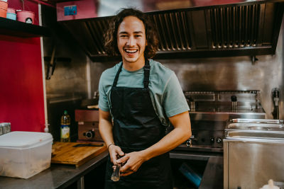 A person in a black apron in a restaurant kitchen.