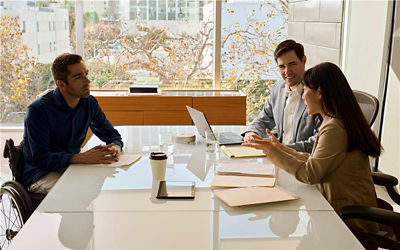 Three individuals seated at a conference table, engaged in discussion with a laptop open in front of them.