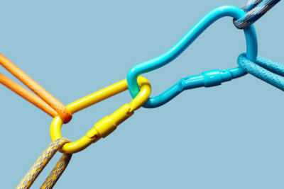 Close-up of a yellow metal link chained to a turquoise metal link, with each link joined to two other chain segments.