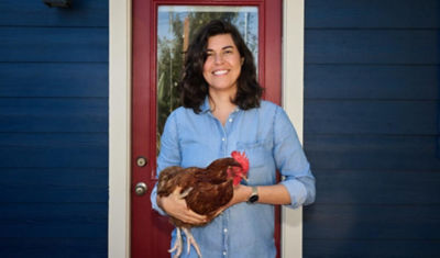 A woman in a blue shirt holding a chicken.