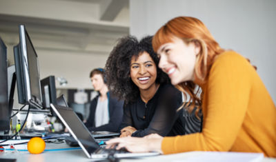 Two colleagues smiling as they review information on a laptop computer